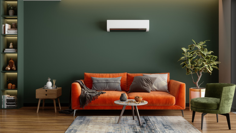 A minimalist living room is painted green with an orange couch.