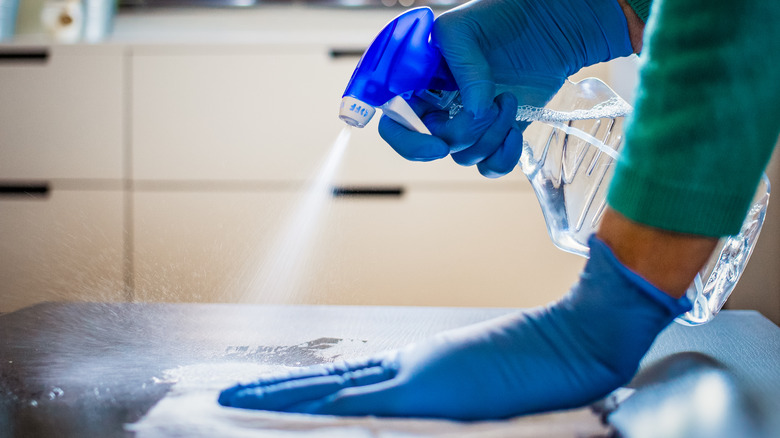 person sanitizing countertop with bleach