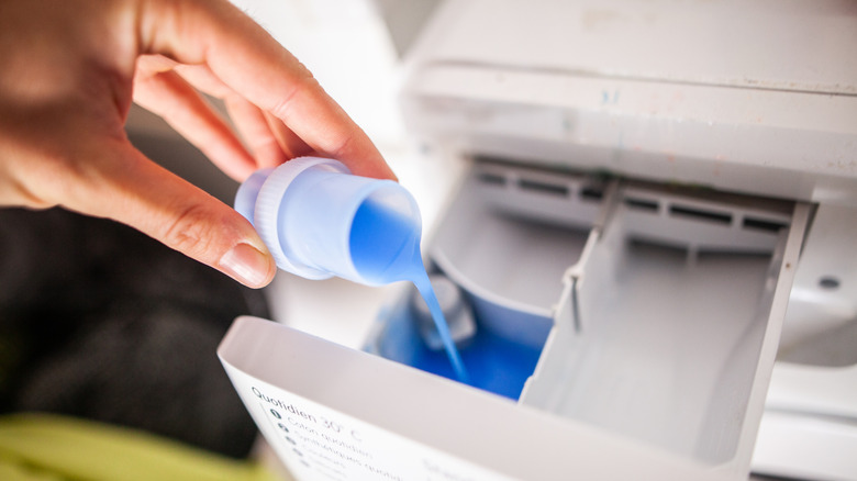 A hand pours a small capful of laundry additive in the washing machine compartment