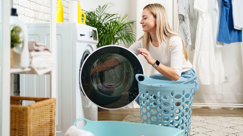 Woman loading laundry into a washing machine, clothes hung behind her