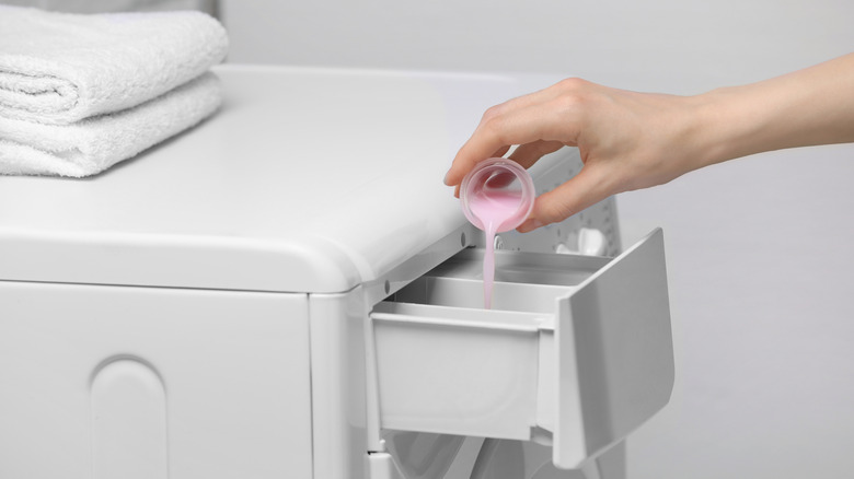 Woman's hand pours pink fabric softener into washing machine compartment