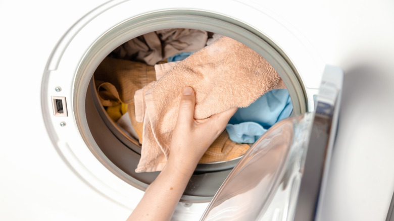 Person placing towel in washing machine with clothing