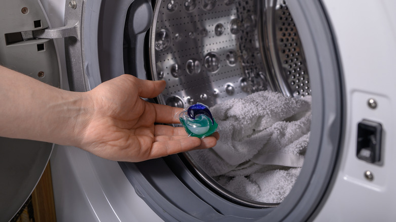 Person holding laundry pod in front of towels in washing machine