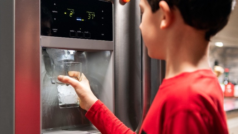 A child getting ice from a refrigerator ice maker