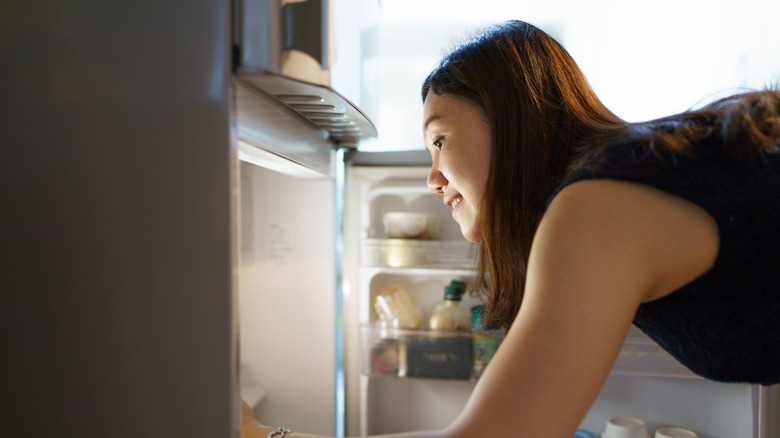 Woman getting food out of a traditional top-freezer fridge.