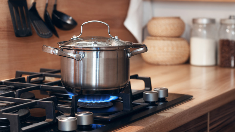 stainless steel pan on a gas hob with spices and kitchenware in background