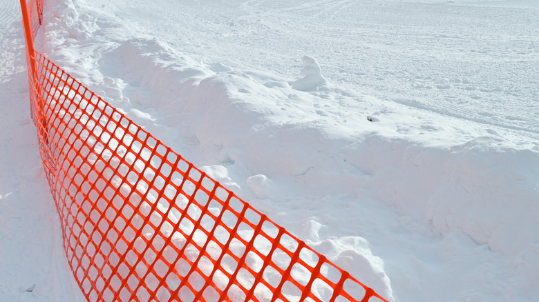 Temporary orange grid snow fencing with snow on the ground and accumulated on one side of the fence