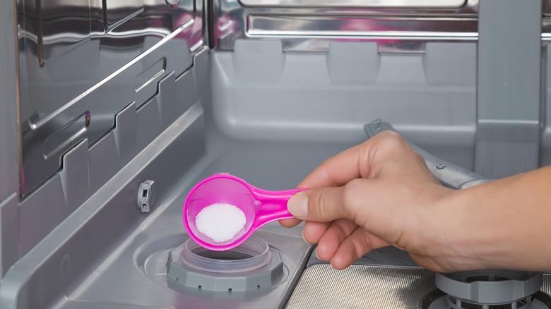 Hand using pink scooper to pour dishwasher salt into dishwasher