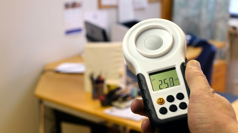 Person measuring lumens in an office using a handheld lux meter