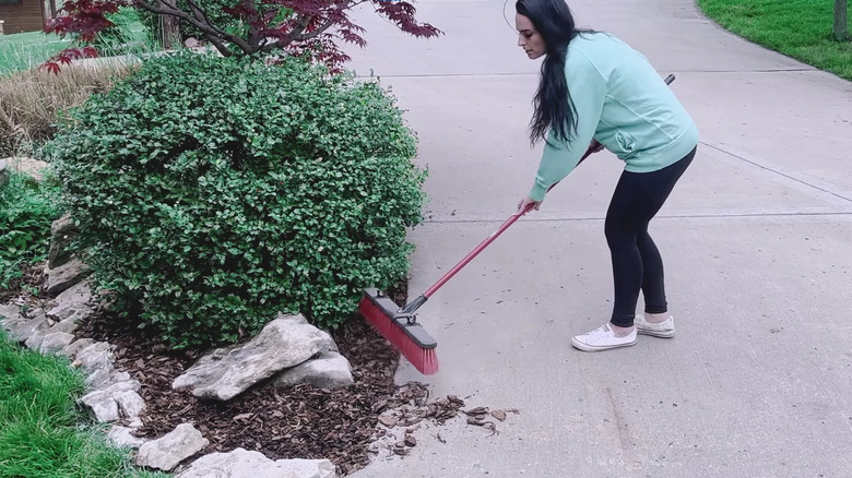 Woman sweeping mulch off driveway