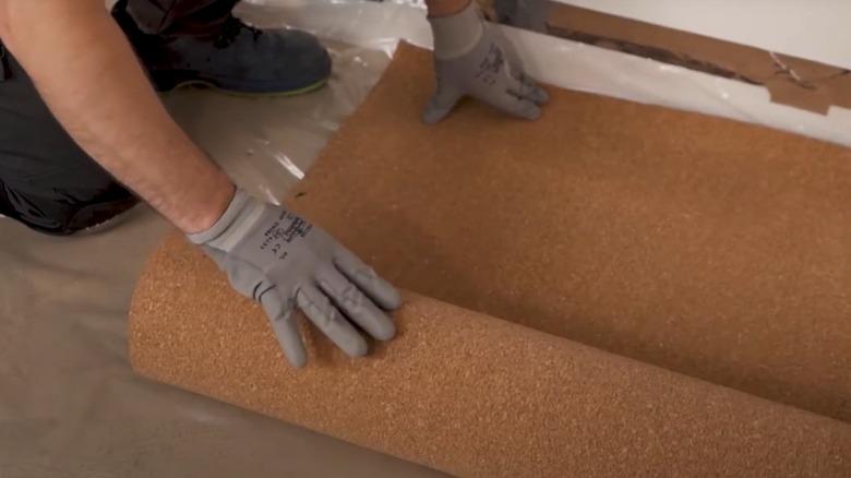 Person installing cork underlayment over vapor barrier