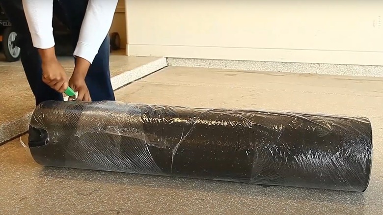 Person unwrapping roll of rubber underlayment