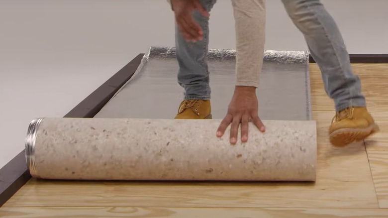 Person rolling foam underlayment over plywood subfloor