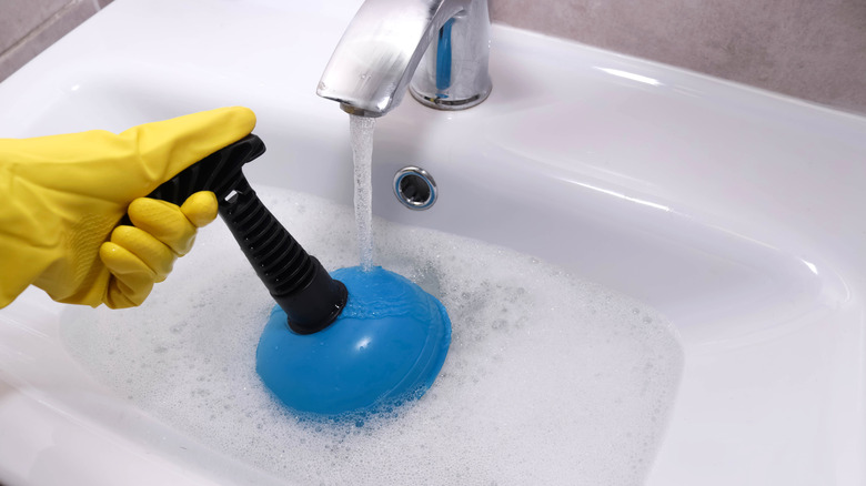 Person unclogging sink with overflow drain with plunger