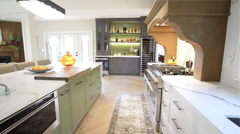 Kitchen with white quartz countertops, green and dark brown cabinetry, brown details, and wood herringbone flooring