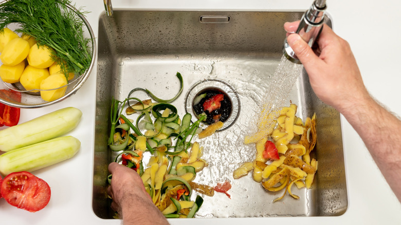 A person rinses food scraps down a kitchen sink