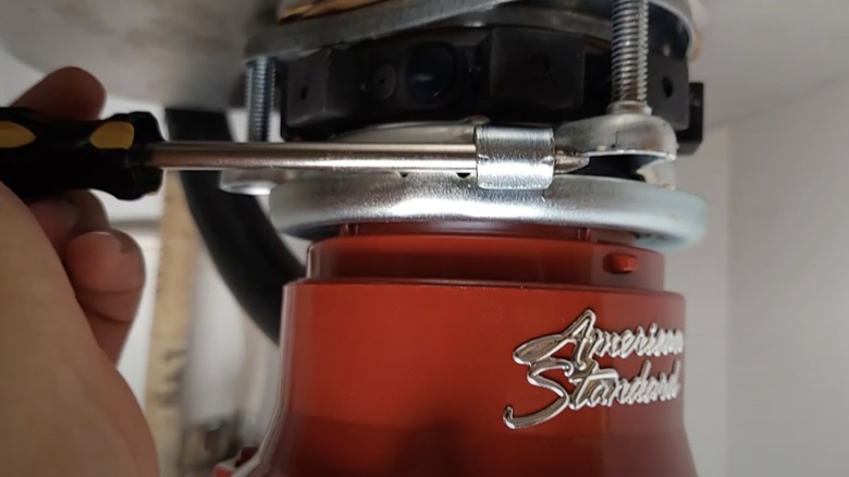 A person uses a screwdriver to attach a garbage disposal to a mounting ring