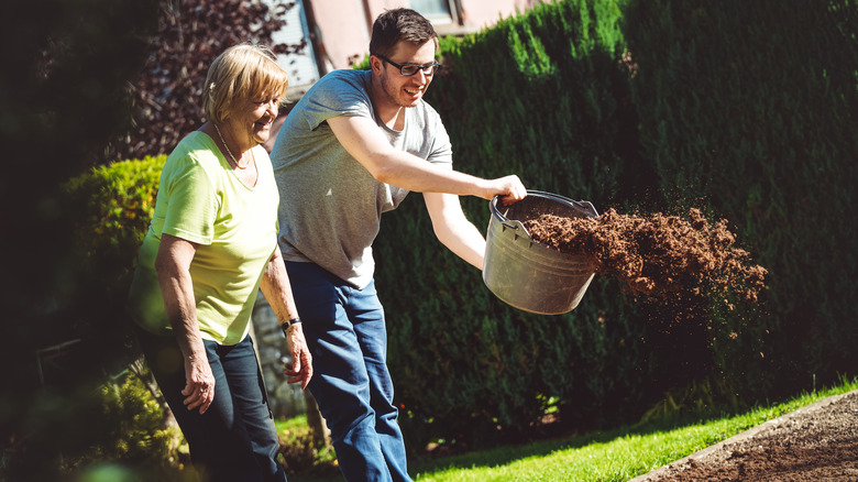 Two people toss compost onto the ground