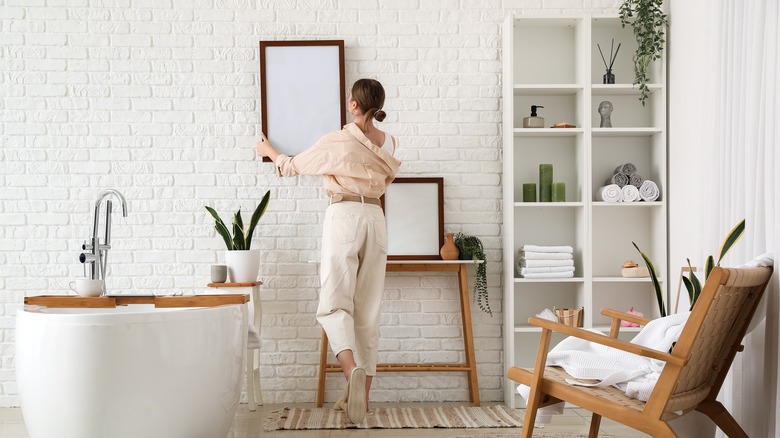 Woman hanging blank framed canvases in bathroom