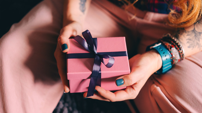 Person holding a pink gift box with a dark blue ribbon.