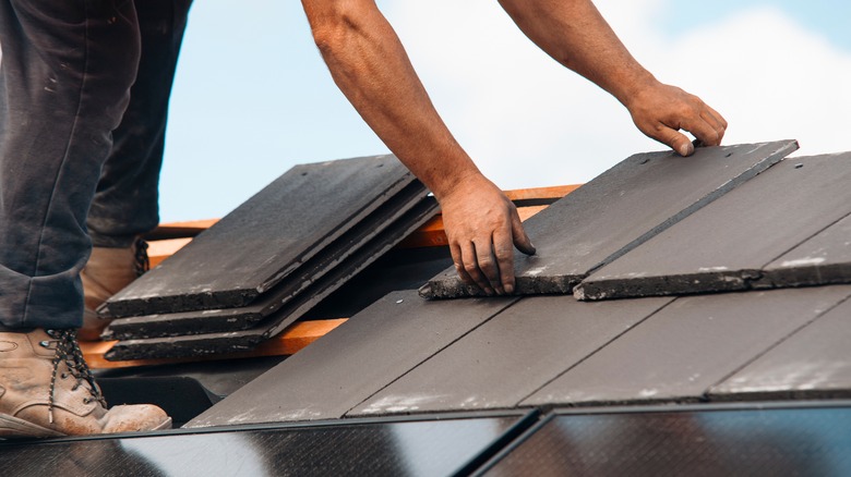 A worker installing slate tiles on a roof