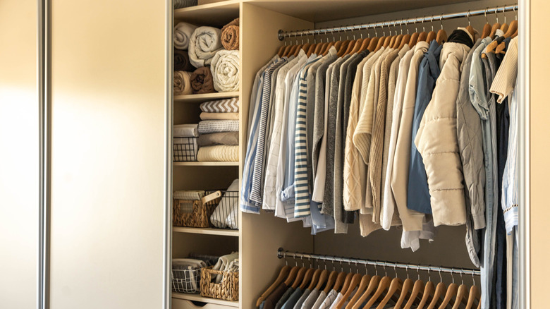 open reach-in closet with sliding door showing clothes on 2 levels of hangers and shelving unit