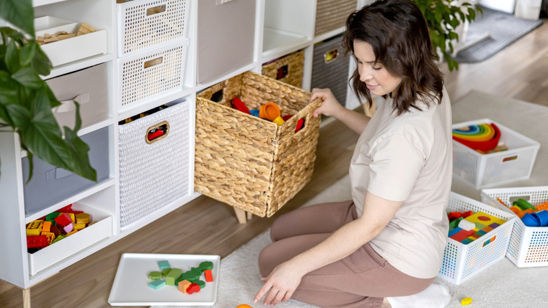 A smiling mom is organizing children's toys in bins.