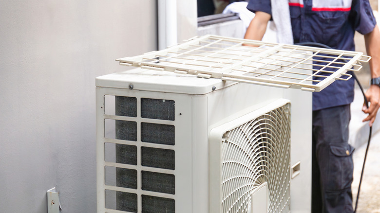 A professional cleaning an external AC unit