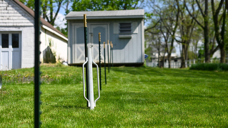 Manual fence post driver by metal posts in green yard