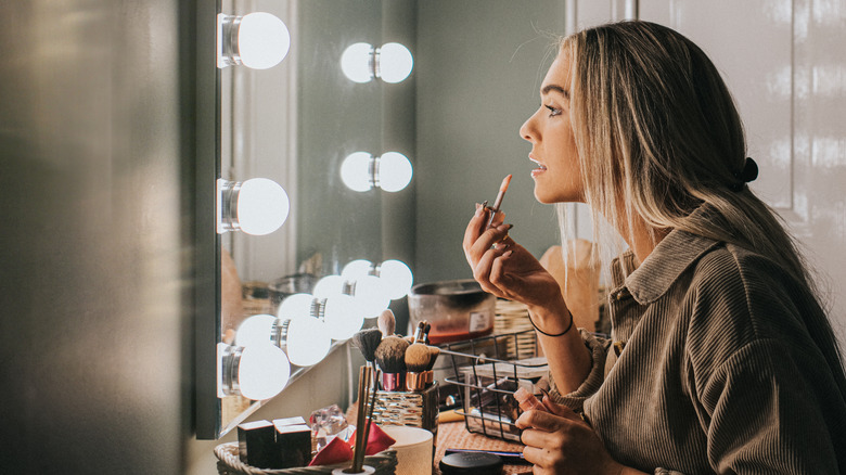 A woman applies makeup at a vanity with lights