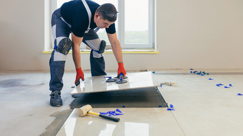 A professional man installing white ceramic floor tile