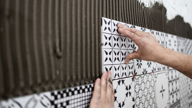 Person installs ceramic tiles on wall.