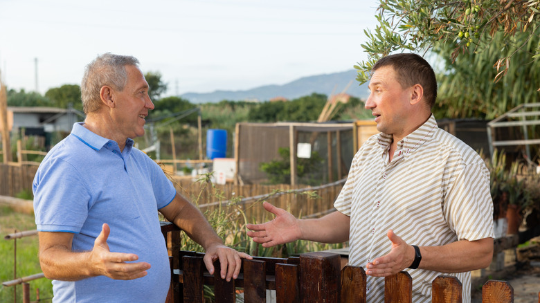 two men talking over a wood fence