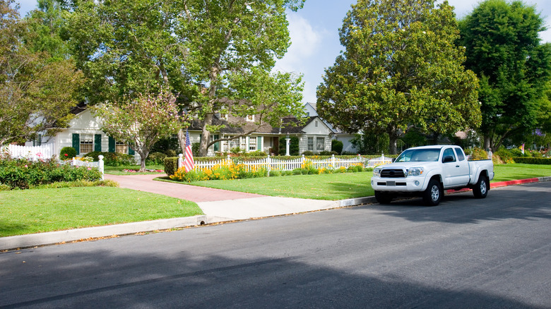 white truck parked next to a curb in front of a home and fenced yard