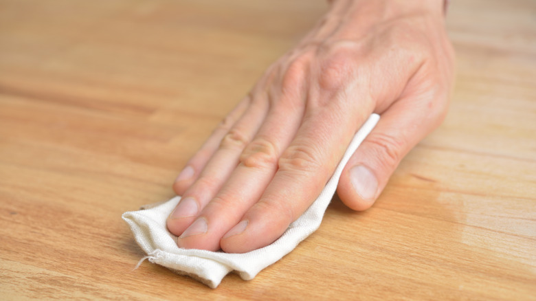 person rubbing oil on wood with cloth