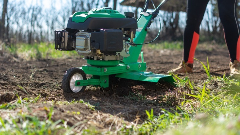 Woman pushing green garden tiller 