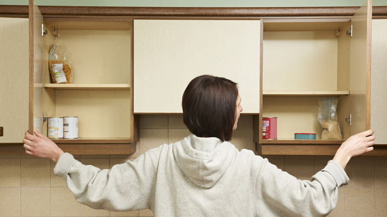 A woman standing in front of a row of open kitchen cabinets