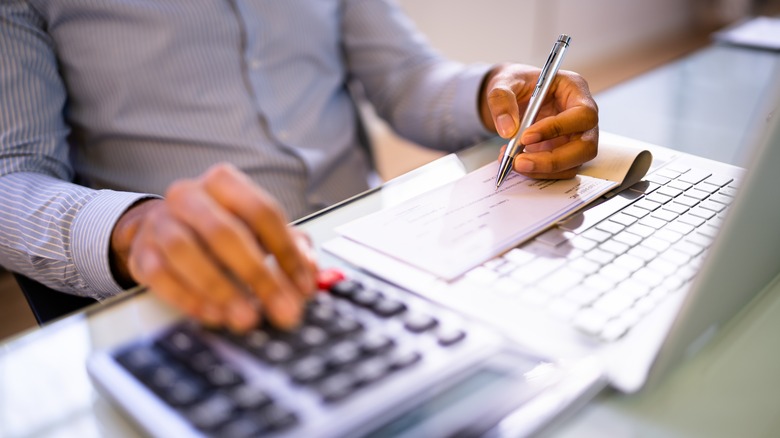 Person writing check next to calculator