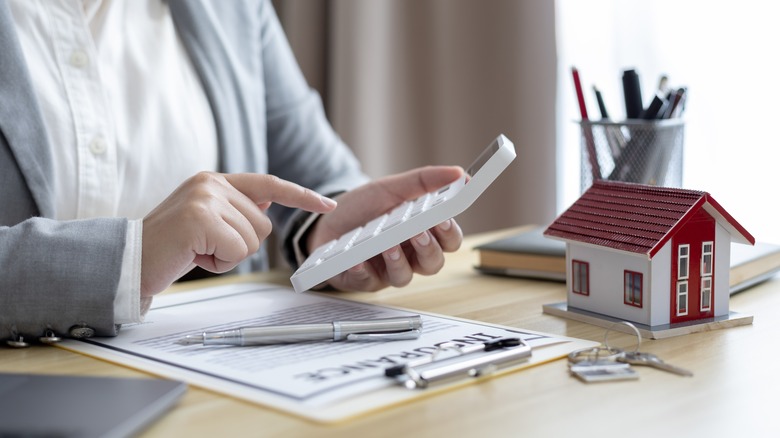 Person holding calculator near mini house