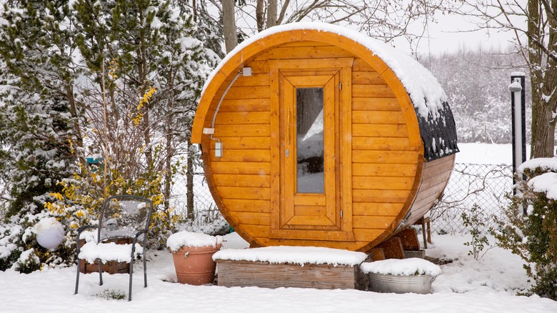 Round barrel sauna in the snow surrounded by trees