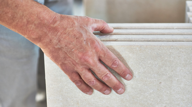 A person thumbing through multiple slabs of white granite