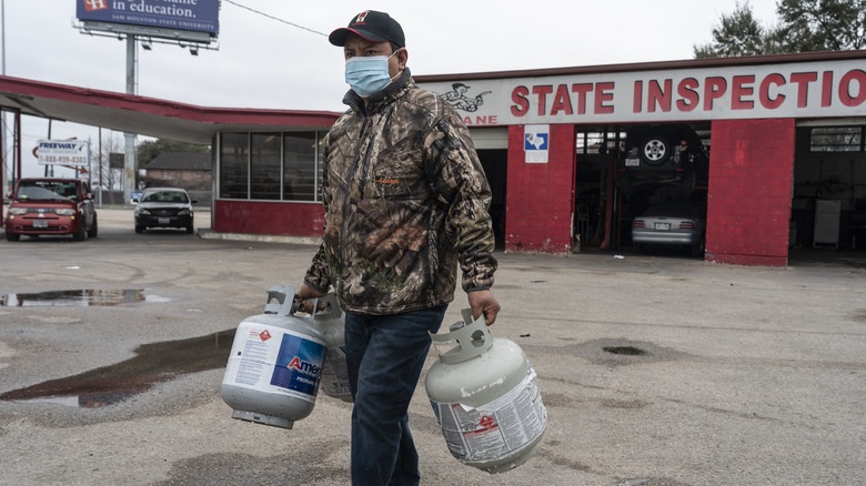 A man carrying two empty propane tanks