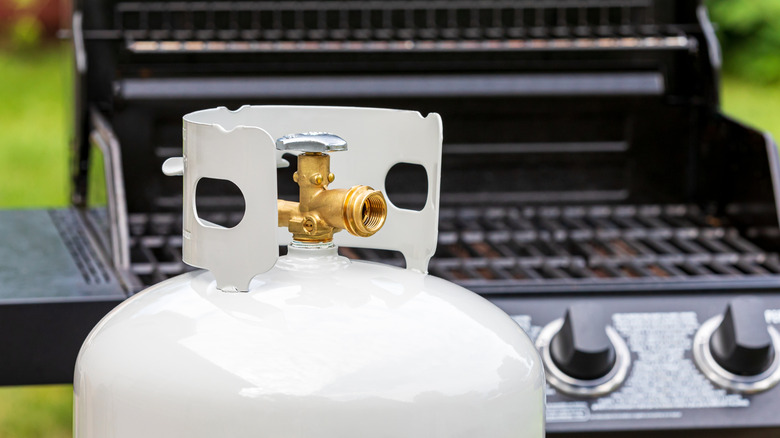 A white propane tank sitting in front of a gas grill