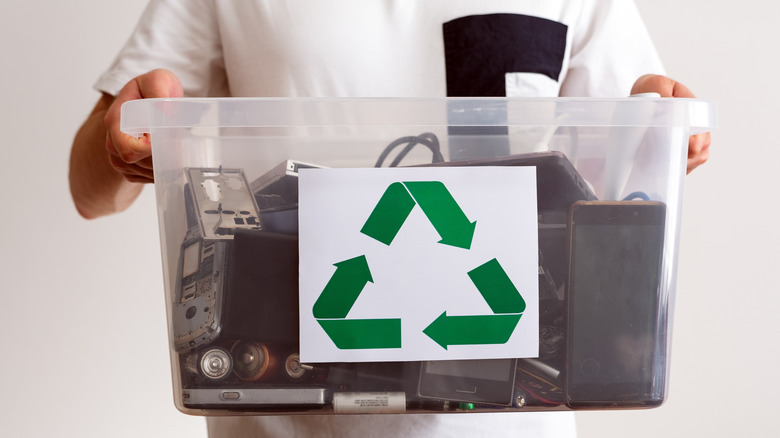 A man holding an assortment of electronic devices and batteries in a recycle bin