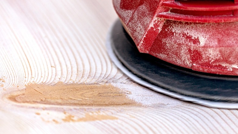 Red orbital sander sanding board with wood filler in knot