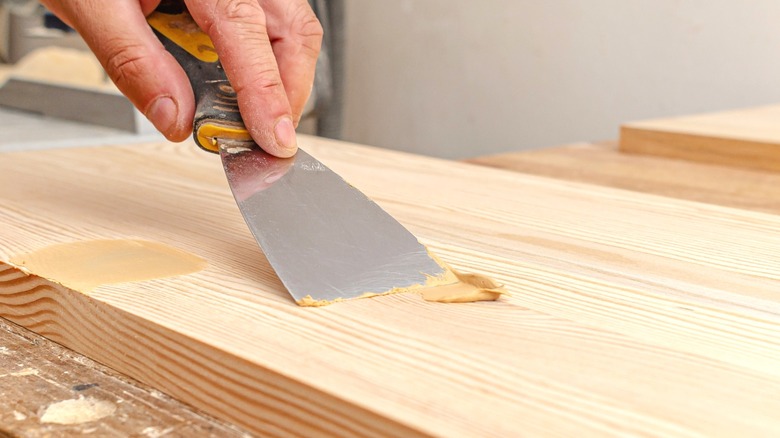 Man smoothing wood filler into unfinished wood board with putty knife