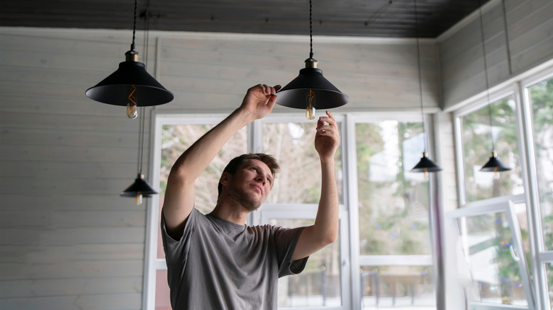 A man changing a light bulb in a pendant light fixture