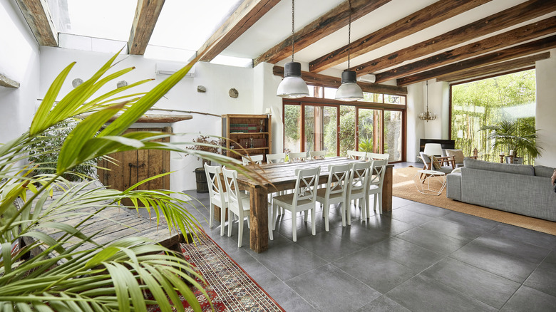 A large open room with high ceilings, wood beams, low hanging lights, and houseplants.