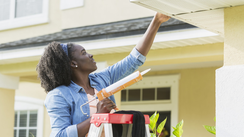 Woman caulking a gap on a house