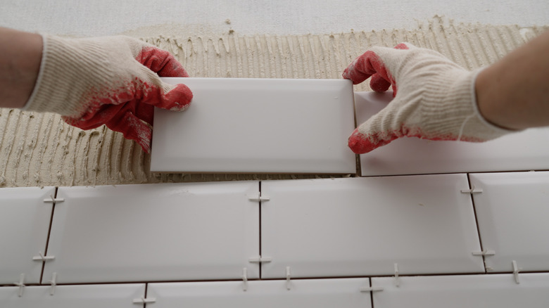 Gloved hands laying backsplash tile with spacers